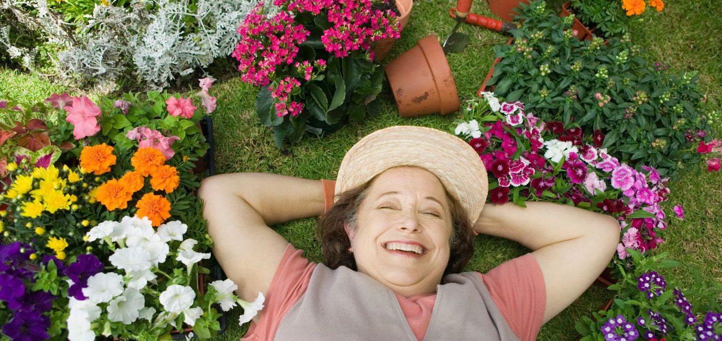 Eine lächelnde Frau liegt auf dem Rasen, umgeben von vielen Blumen.