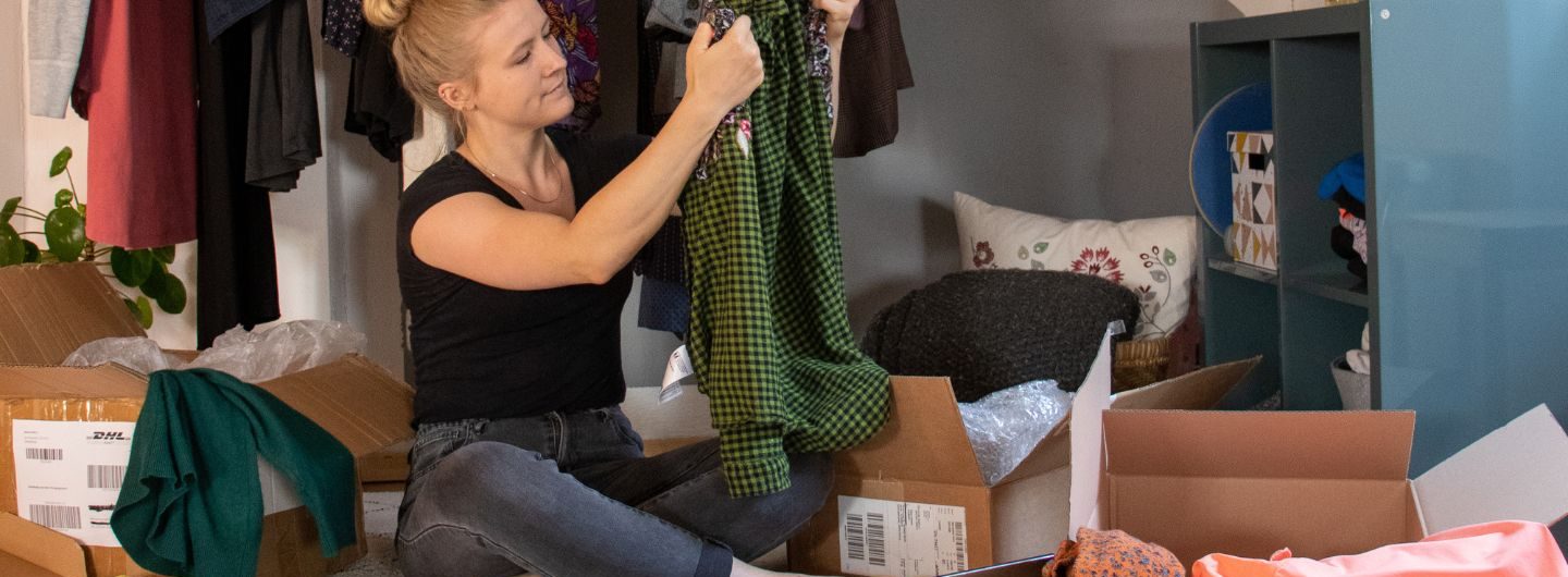 Eine Frau sitzt zuhause und schaut sich ein Kleidungsstück an, dass sie online bestellt und gerade ausgepackt hat_Raus aus dem Retouren-Wahnsinn