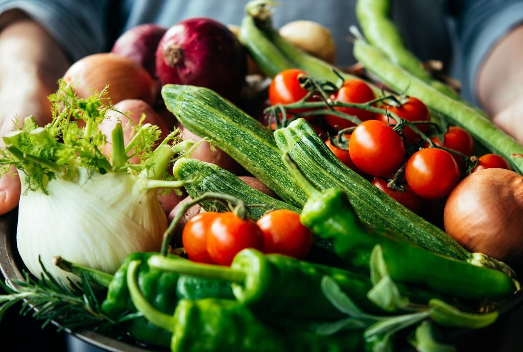 Ein Korb voller Gemüse wird von zwei Händen getragen.