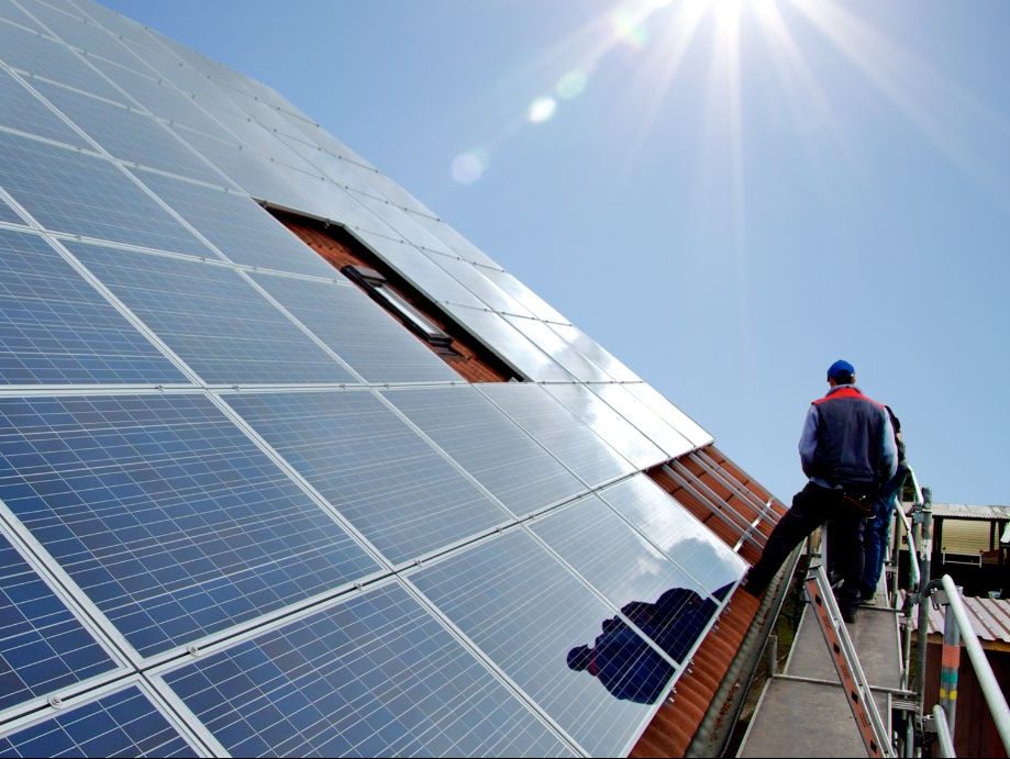 Das Bild zeigt einen Menschen neben einer Photovoltaik-Anlage auf einem Dach.