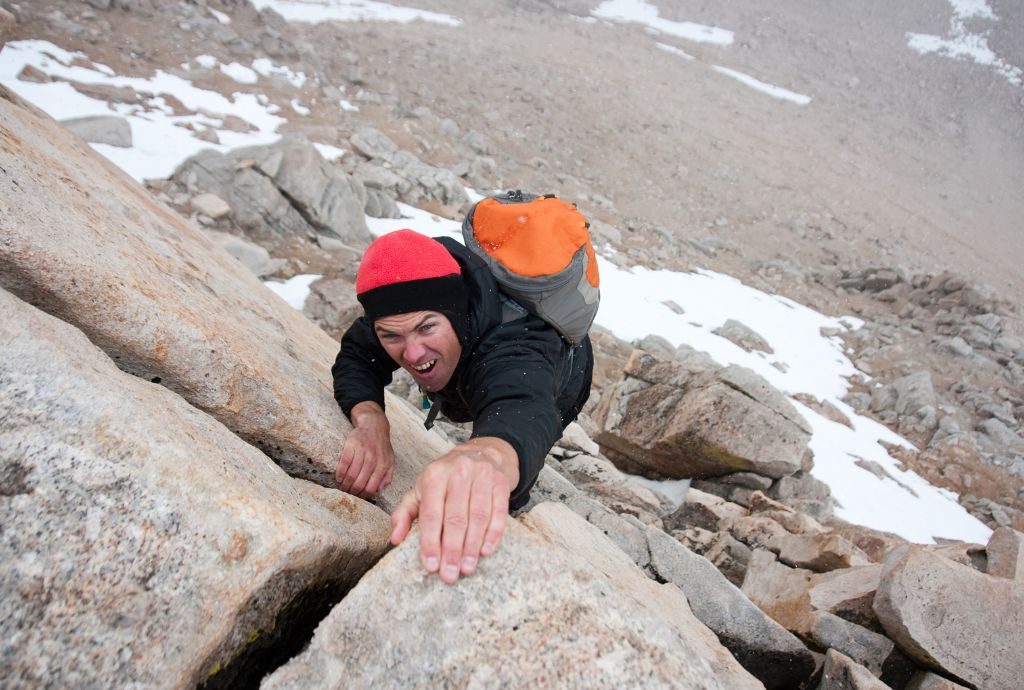 Ein Bergsteiger erklimmt einen Berg und zeiht sich an den Händen hoch.