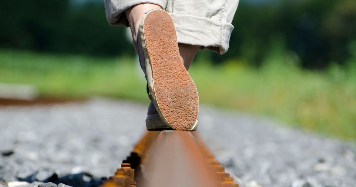 Ein Mensch läuft eine Bahnschiene entlang, es sind nur die Füße zu sehen.
