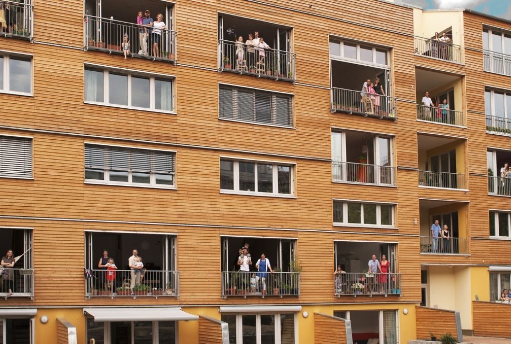Sanieren mit Herz: Das Bild zeigt ein Mehrfamilienhaus in Holzbauweise mit Balkonen, auf denen Menschen stehen.