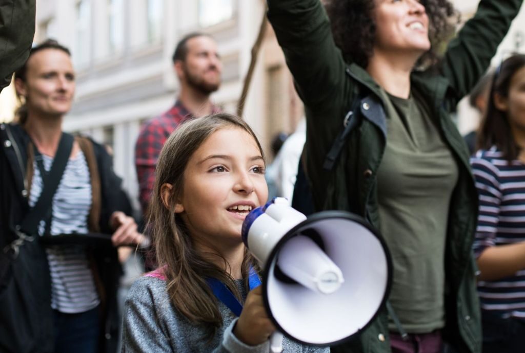 Eine Gruppe von Menschen demonstriert, ein Mädchen im Vordergrund hält ein Megaphon in der Hand.