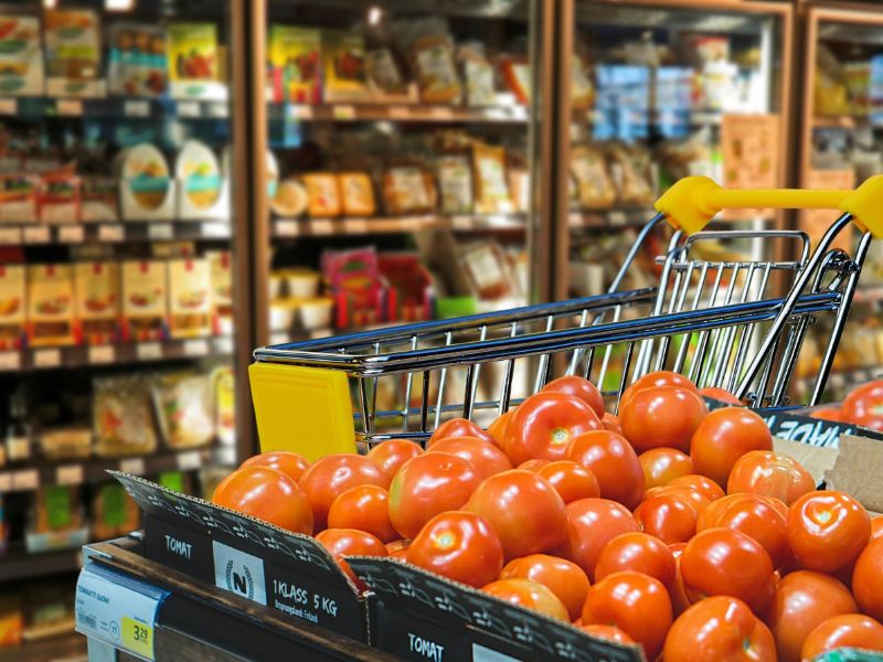Das Bild zeigt Tomaten und Regale voller Waren im Supermarkt.