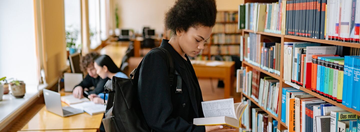 Eine Studentin schaut in der Bibliothek in ein Buch.