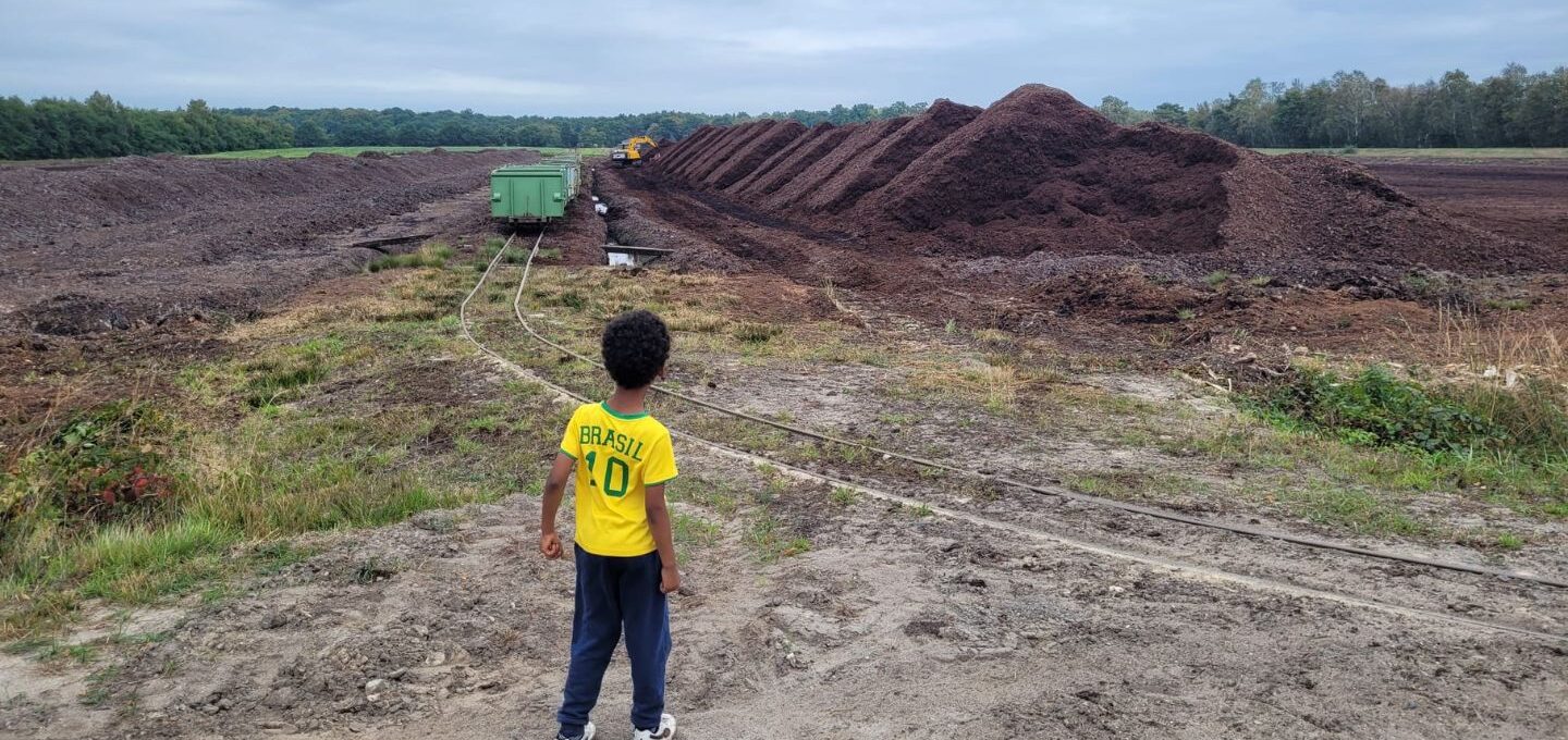 Ein Junge mit Fußballtrikot steht auf einer Fläche, auf der Torf abgebaut wird.