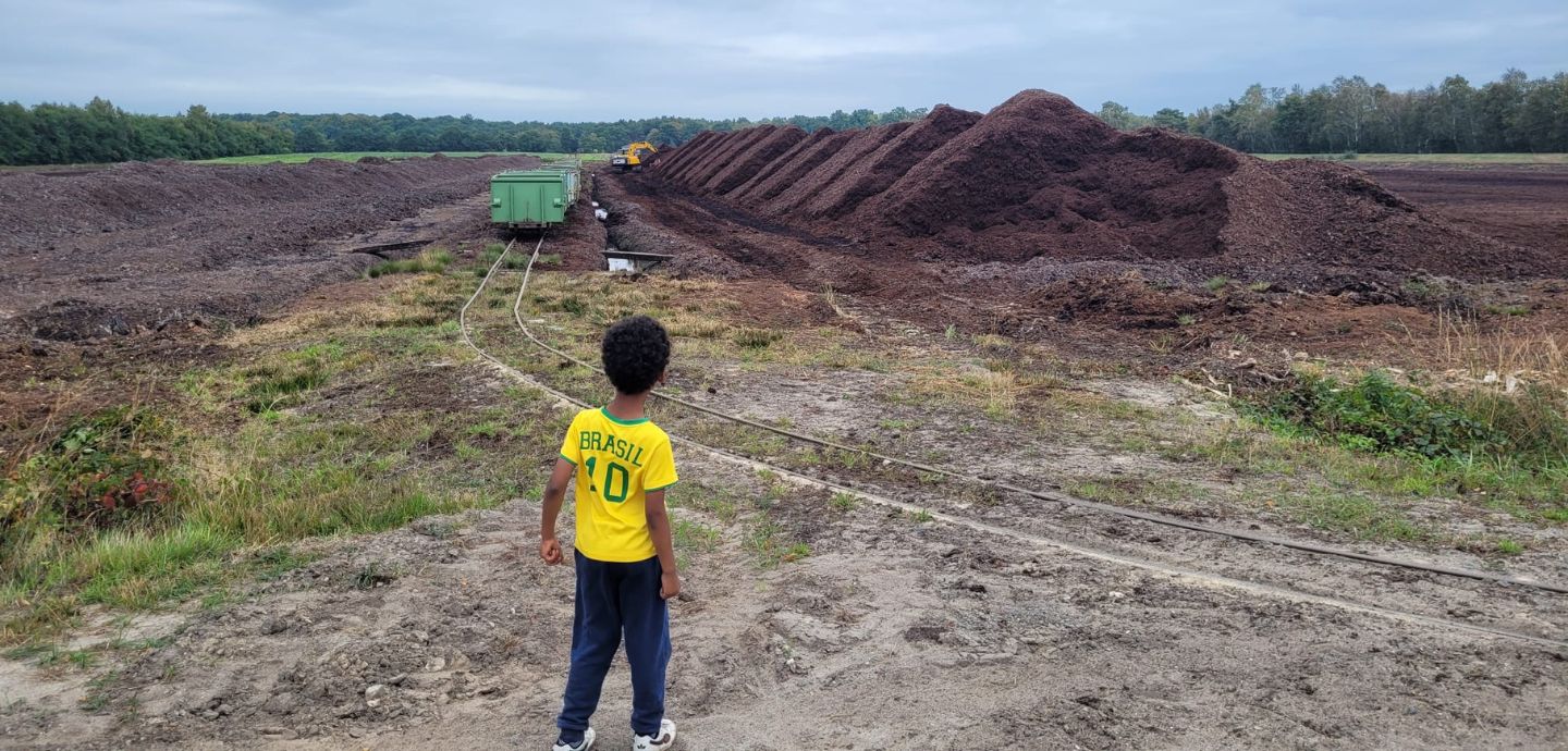 Ein Junge mit Fußballtrikot steht auf einer Fläche, auf der Torf abgebaut wird.