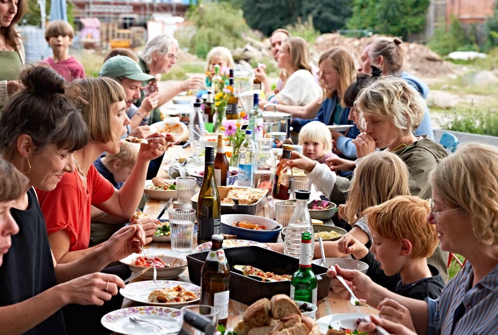 Rund 20 Bewohnerinnen und Bewohner von Hof Prädikow sitzen an einer langen Essenstafel im Freien zusammen.