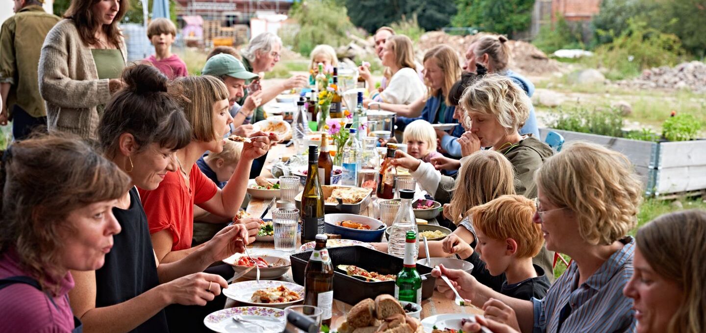 Rund 20 Bewohnerinnen und Bewohner von Hof Prädikow sitzen an einer langen Essenstafel im Freien zusammen.