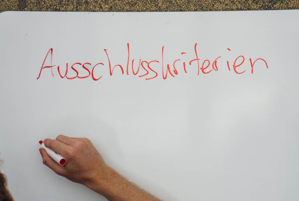 Auf einem Whiteboard steht in Handschrift das Wort Ausschlusskriterien. Darunter ist eine Hand mit Stift, die im Begriff ist zu schreiben.