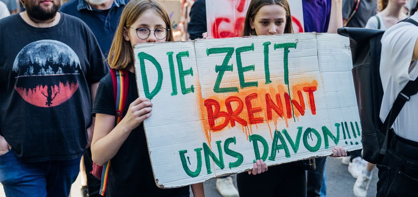 Beim Klimaprotest halten Jugendliche ein Plakat mit der Aufschrift "Die Zeit brennt uns davon" in der Hand.