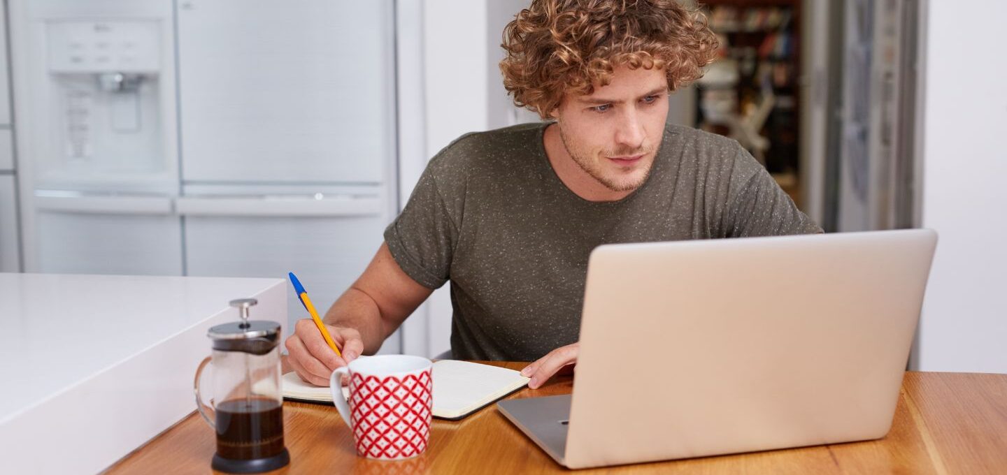 Ein Mann sitzt mit Kaffee vorm Computer und notiert seine Ergebnisse.