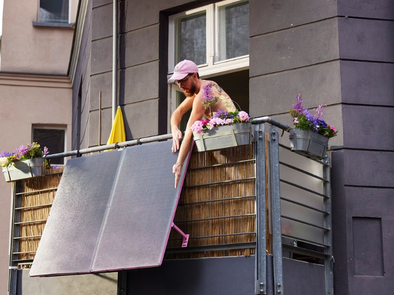 Ein Mann auf einem Balkon hält die Solarmodule eines Balkonkraftwerks in Händen.