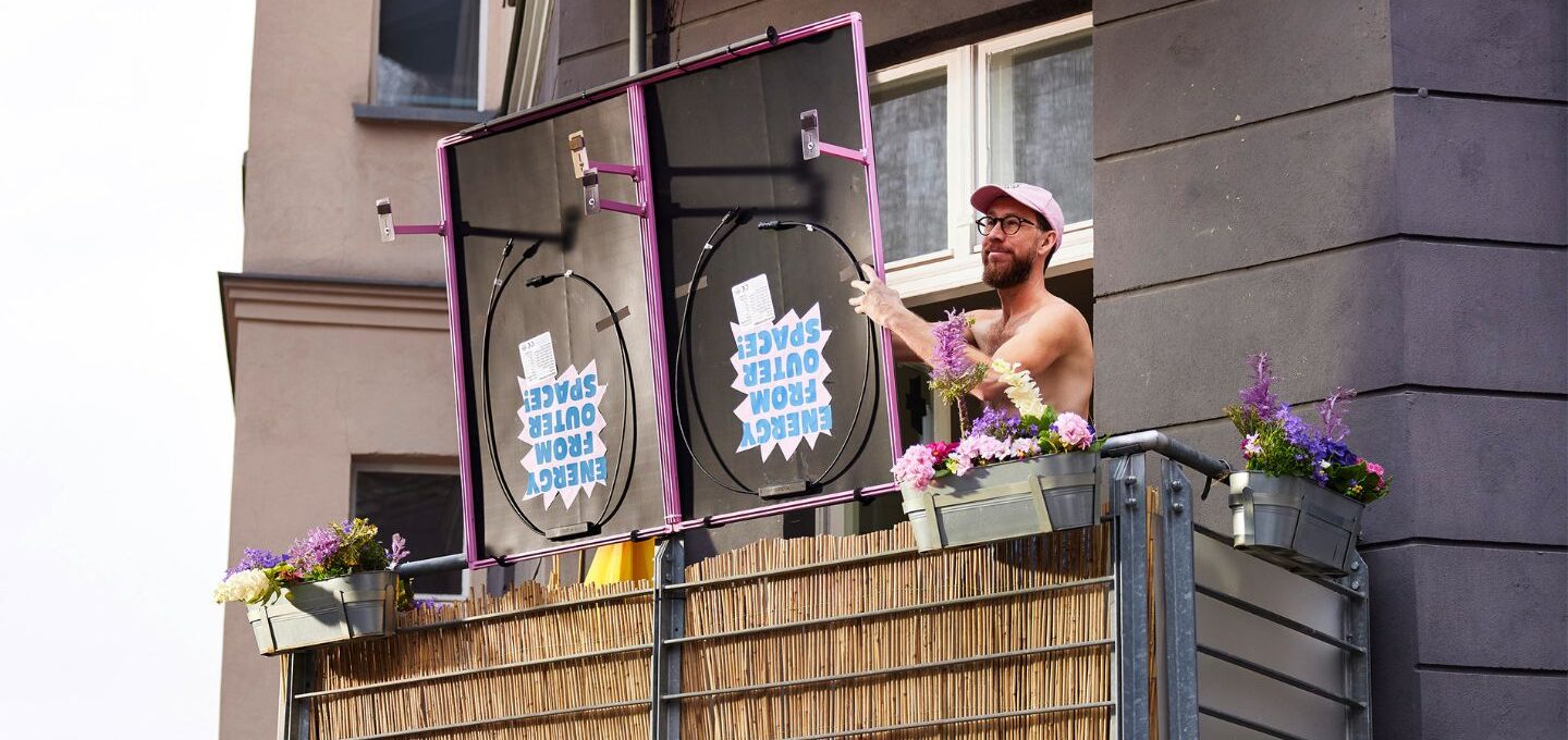 Ein Mann auf einem Balkon hält die Solarmodule eines Balkonkraftwerks in Händen.