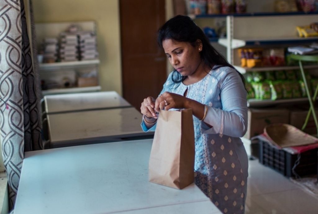 Eine Frau in Indien verpackt in einem kleinen Geschäft Lebensmittel in eine Tüte.