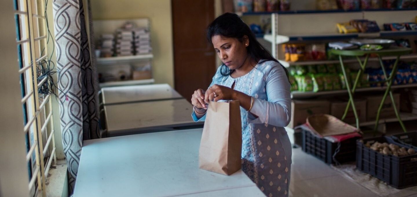 Eine Frau in Indien verpackt in einem kleinen Geschäft Lebensmittel in eine Tüte.