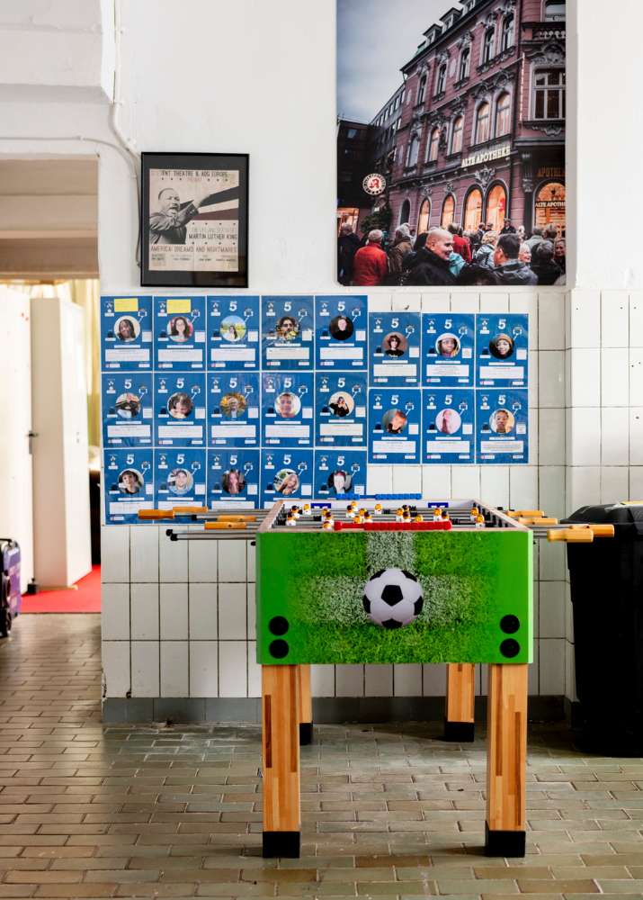 Man sieht einen Tischkicker im Vordergrund und im Hintergrund eine Wand mit den Bildern und Steckbriefen der Jugendredaktion des CORRECTIV.
