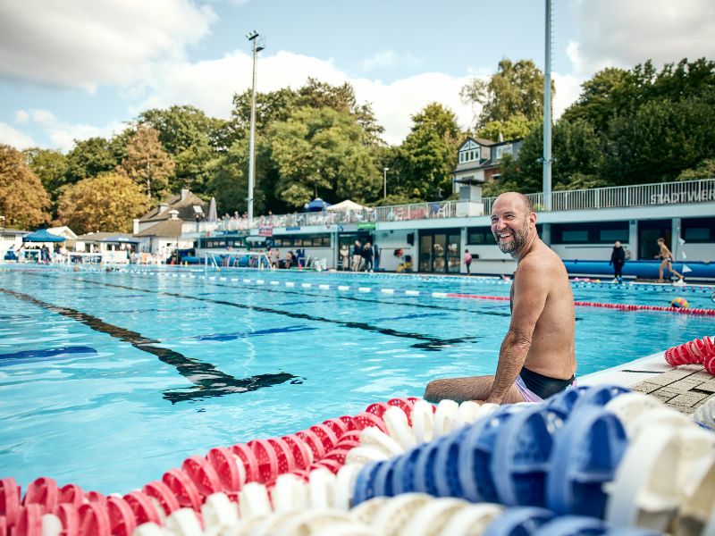 Christoph Baer sitzt am Rand des Schwimmbeckens und lacht in die Kamera.