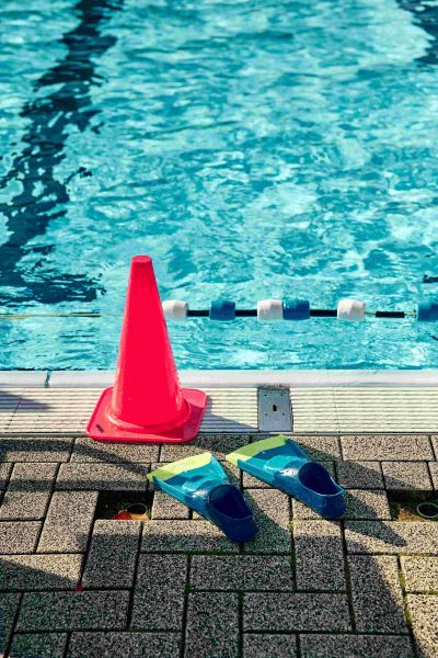 Am Rand eines Schwimmbads stehen Flossen und ein roter Warnkegel.