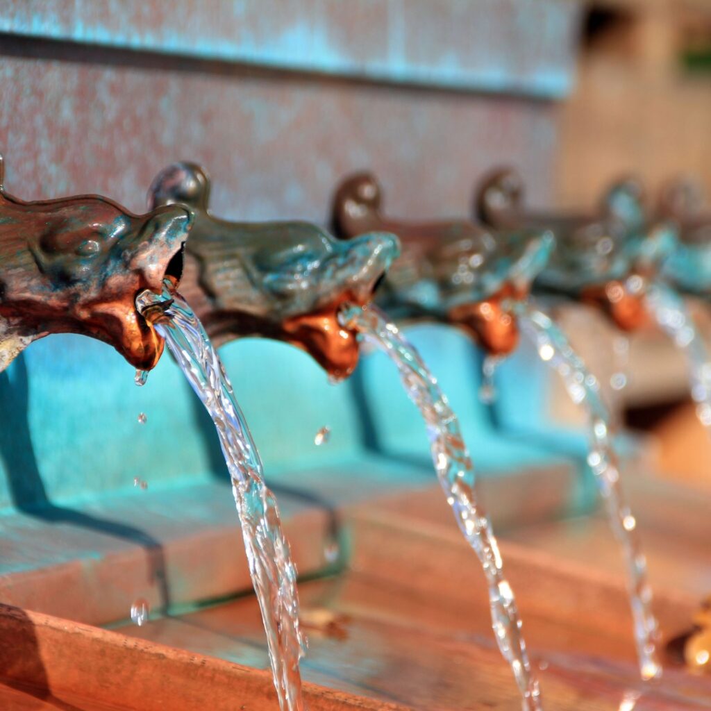 Aus mehreren Wasserspeiern fließt Wasser in Becken.