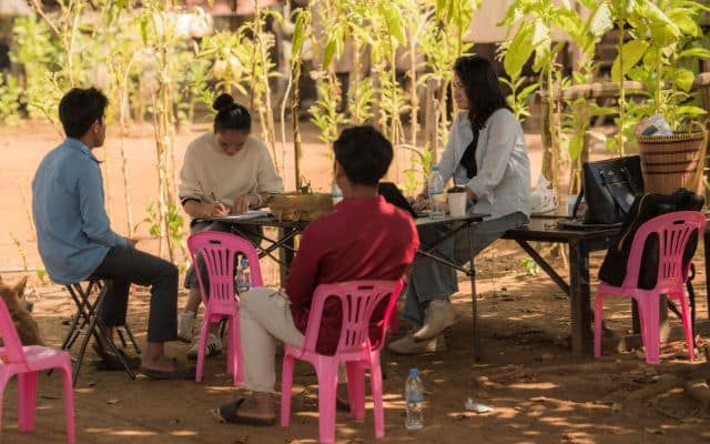 Vier Menschen sitzen im Freien in Kambodscha auf Stühlen und sprechen miteinander.