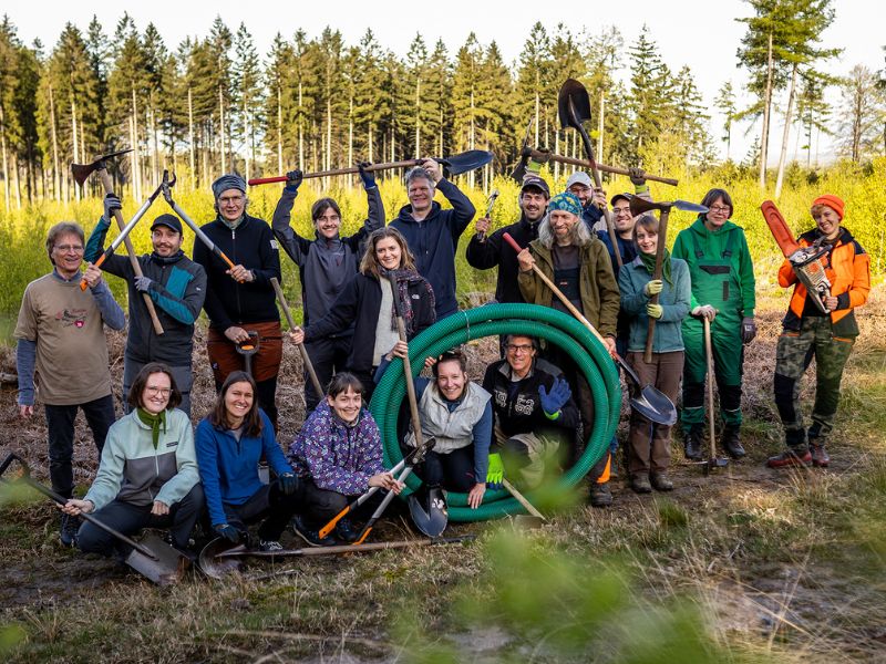 Eine fast 20-köpfige Gruppe von Menschen in der Natur bei einem Arbeitseinsatz.
