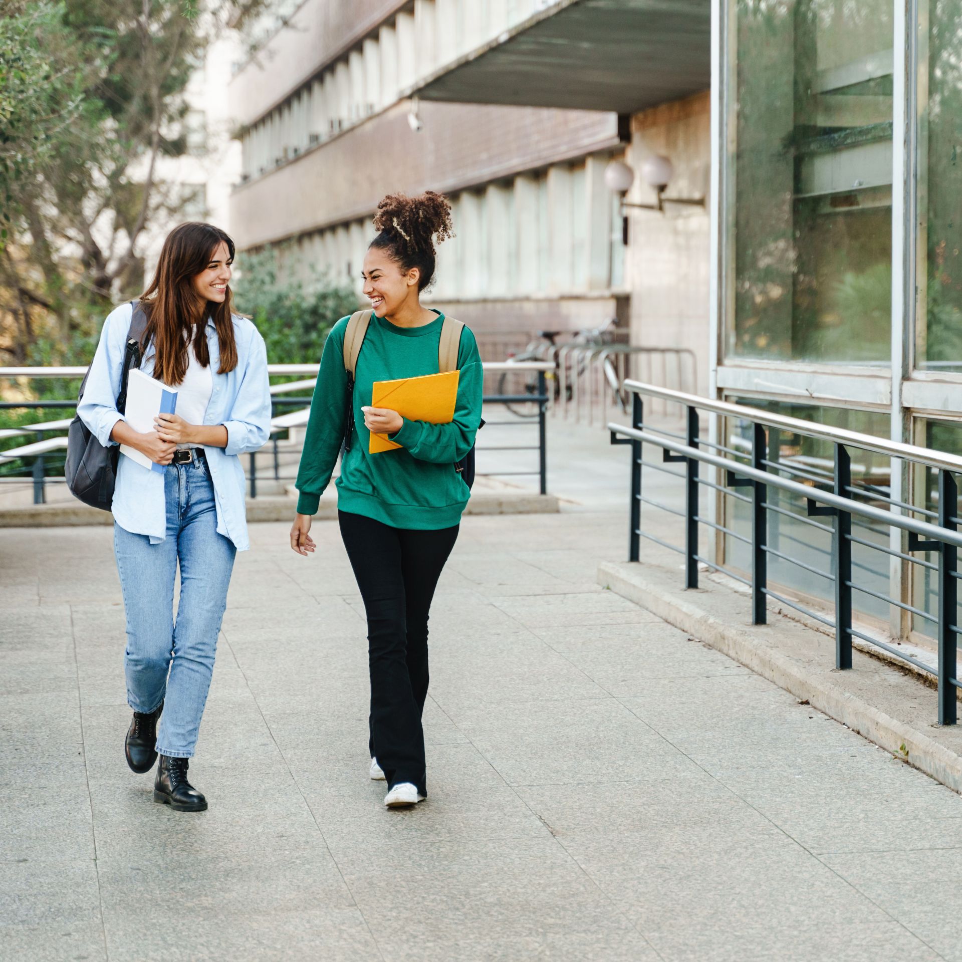 Zwei weiblich gelesene Personen laufen gemeinsam auf einem Campus.